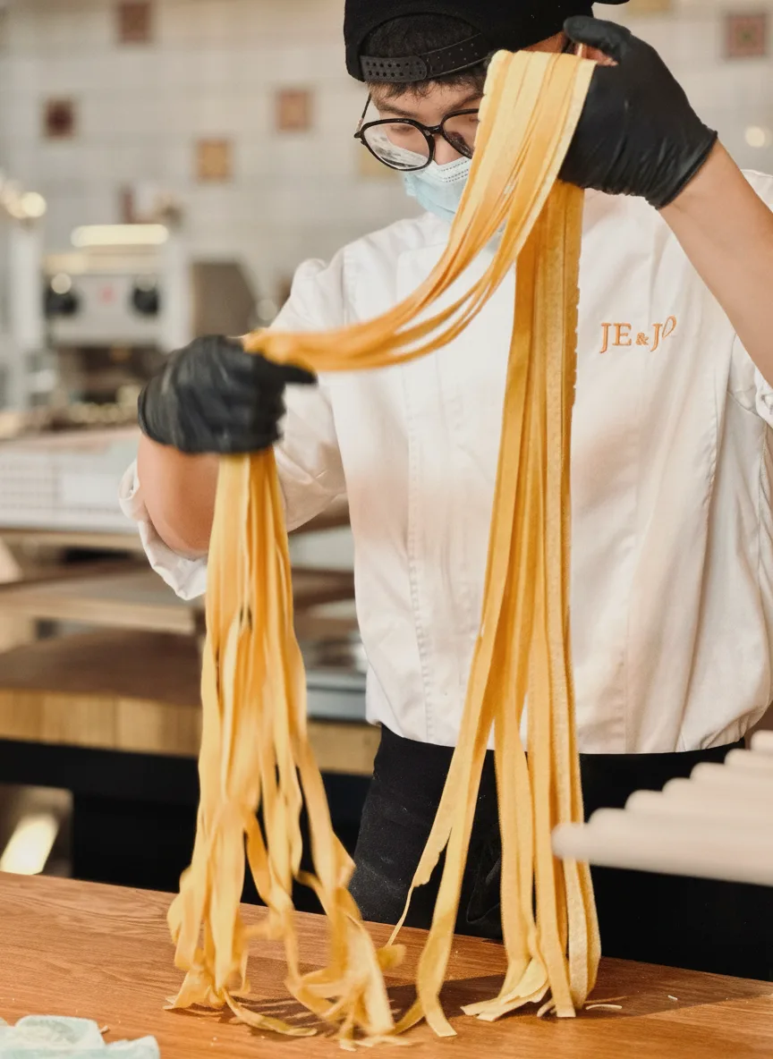 A JE&JO chef lifting a fresh-cut sheet of tagliatelle with both hands